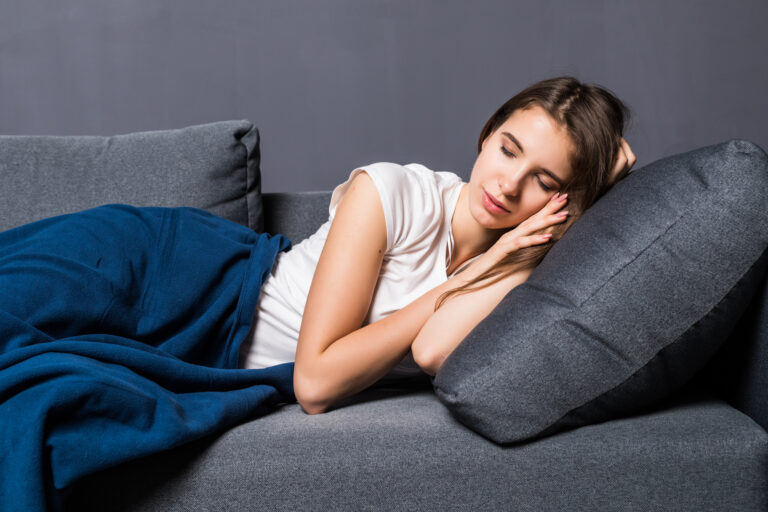 Young girl sleeping on a sofa covered with blue coverlet on gray background