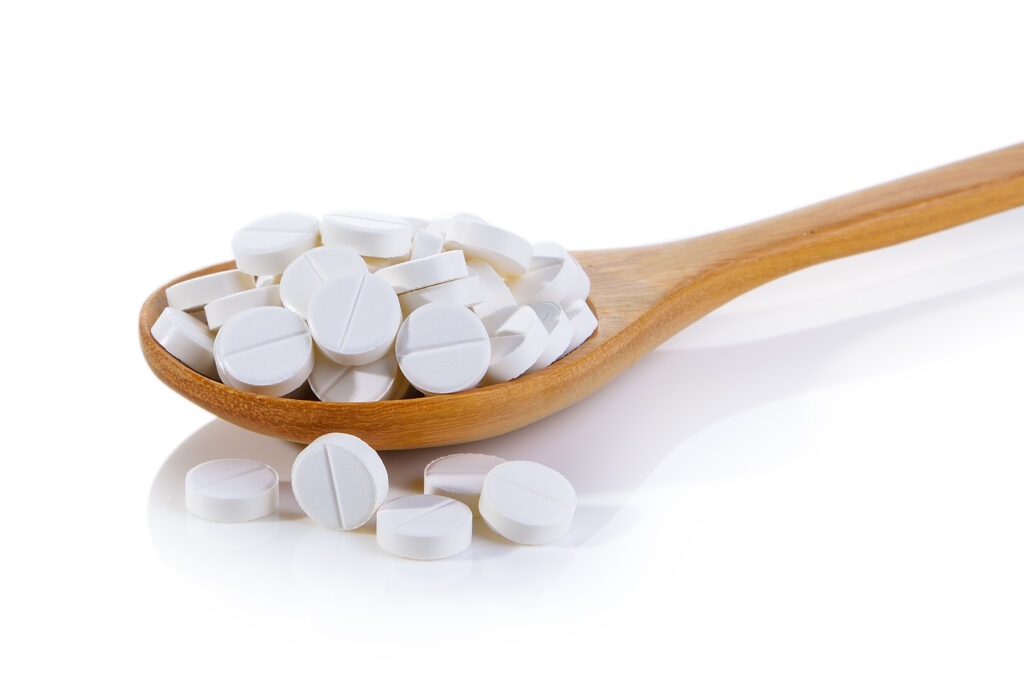 pills in wood spoon on white background